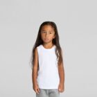 Young child with long hair in a white sleeveless shirt and gray pants standing against gray background.