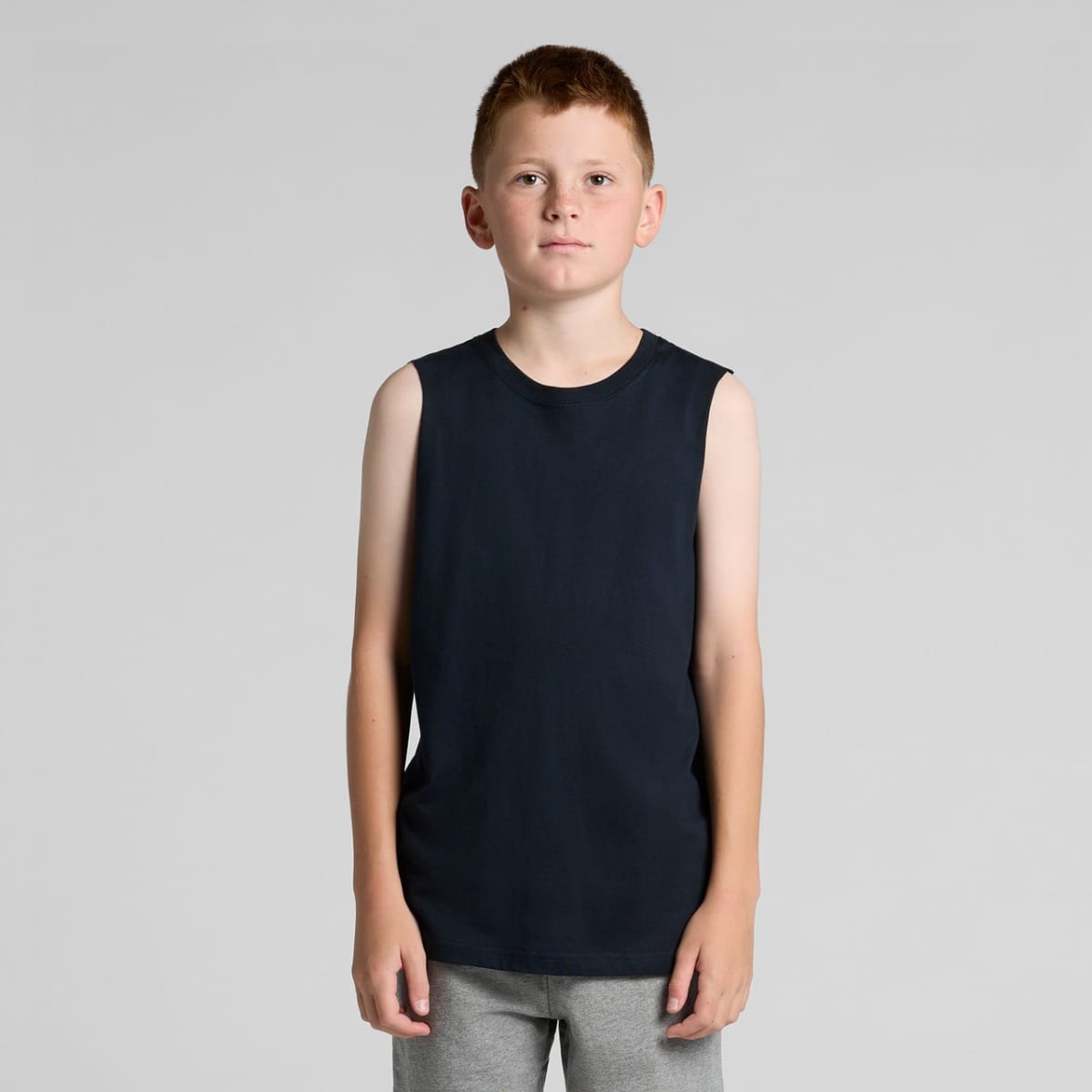 A boy in a black sleeveless shirt and gray pants stands against a plain background.
