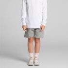 Child in a white long-sleeve shirt, gray shorts, pink socks, and sneakers, standing.
