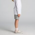 Child in white long-sleeve shirt, gray shorts, and floral shoes standing sideways.