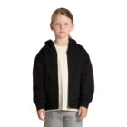 Young child wearing a black zip-up hoodie, beige shirt, and gray pants, standing on white background.