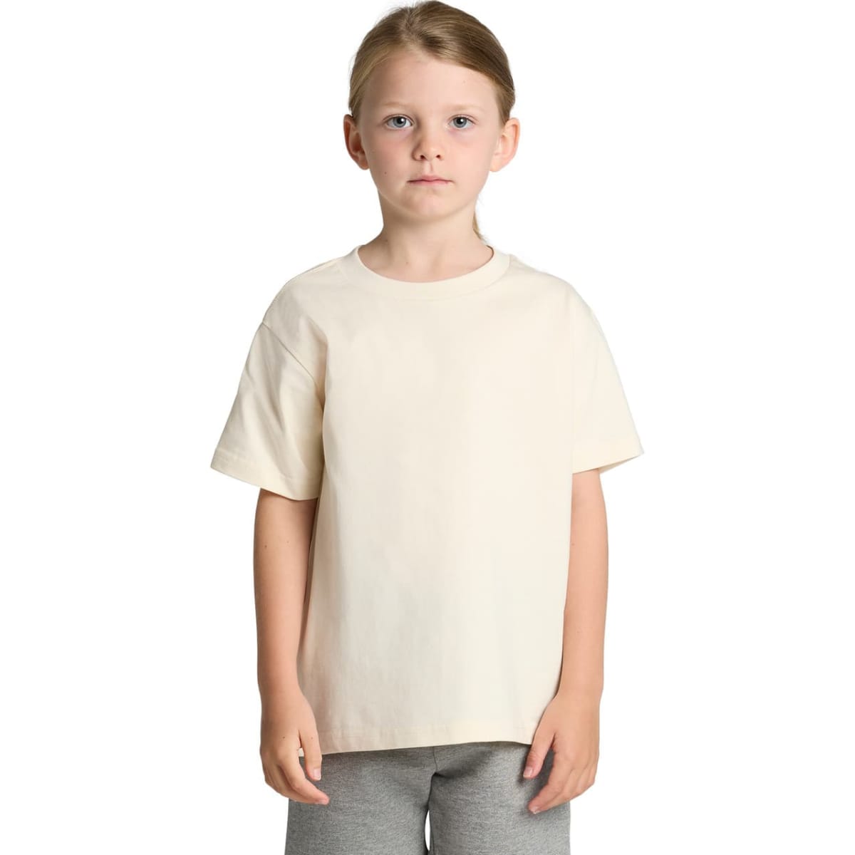 A young child in a plain cream t-shirt and gray pants stands against a white background.