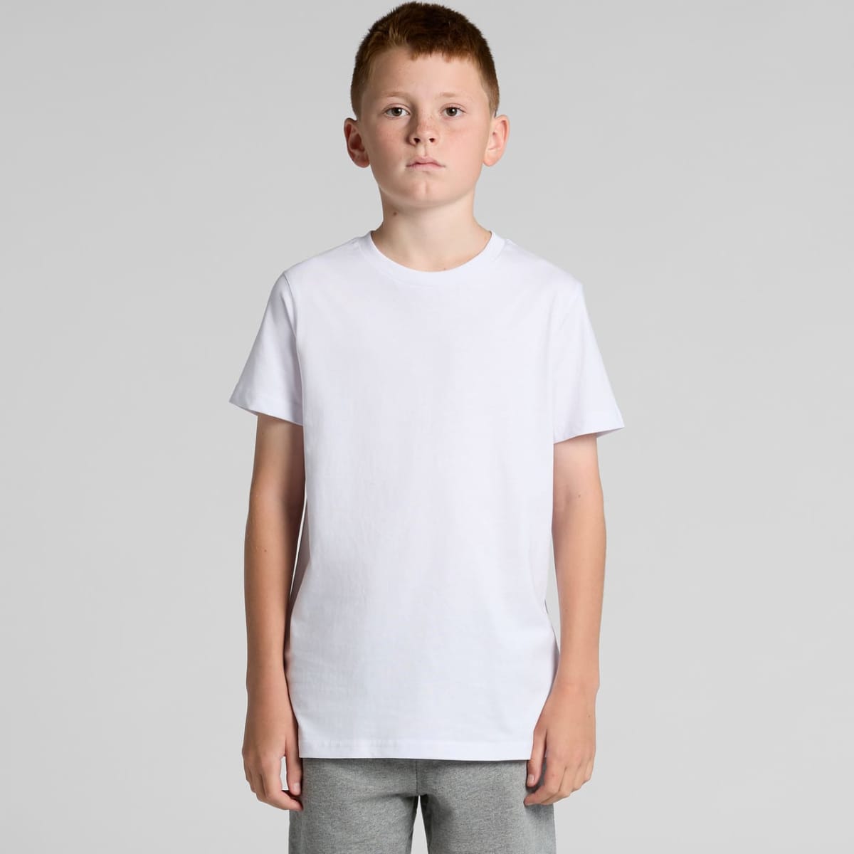 Boy with short hair wearing a plain white t-shirt and gray pants, standing against gray background.