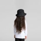 Child with long wavy hair, white shirt, and black bucket hat facing away against gray background.