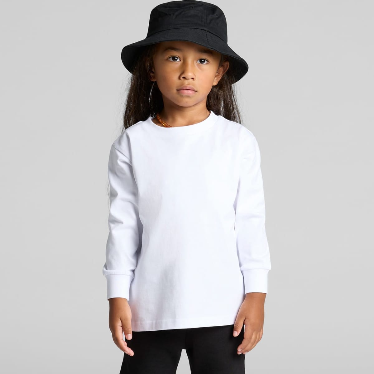 Child in a white long-sleeve shirt, black pants, and a black bucket hat, standing neutral.