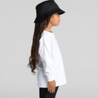 Child in a white long-sleeve shirt and black hat standing sideways against a plain background.