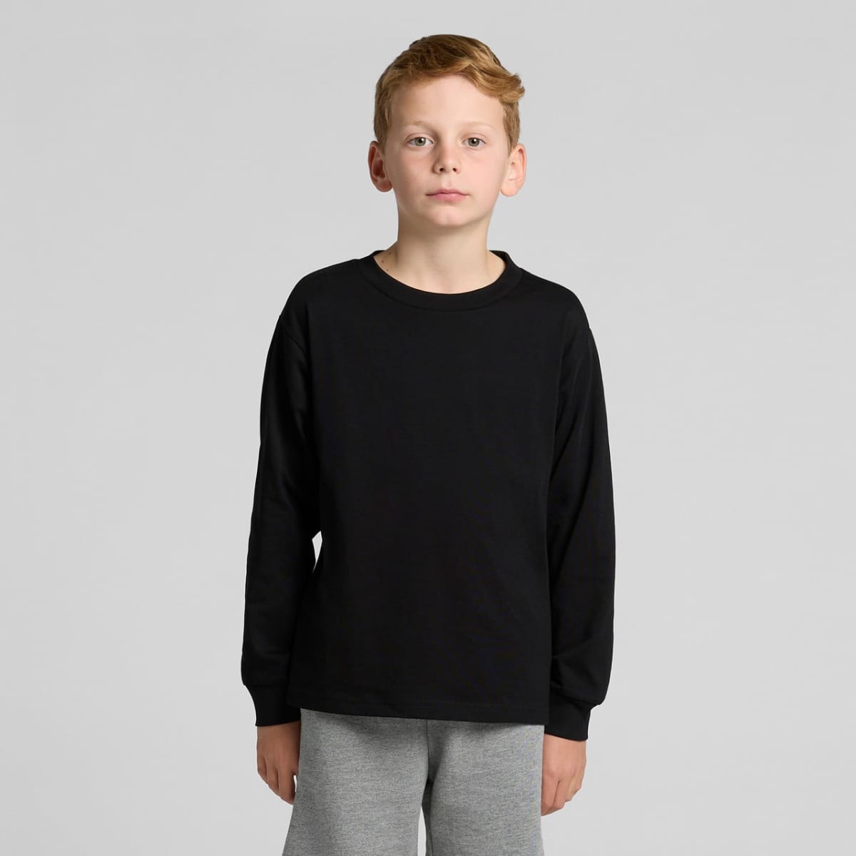 Boy with short blond hair wearing a black long-sleeve shirt and gray pants, standing.