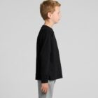 Young boy in a black long-sleeve shirt and gray pants standing in profile against gray background.
