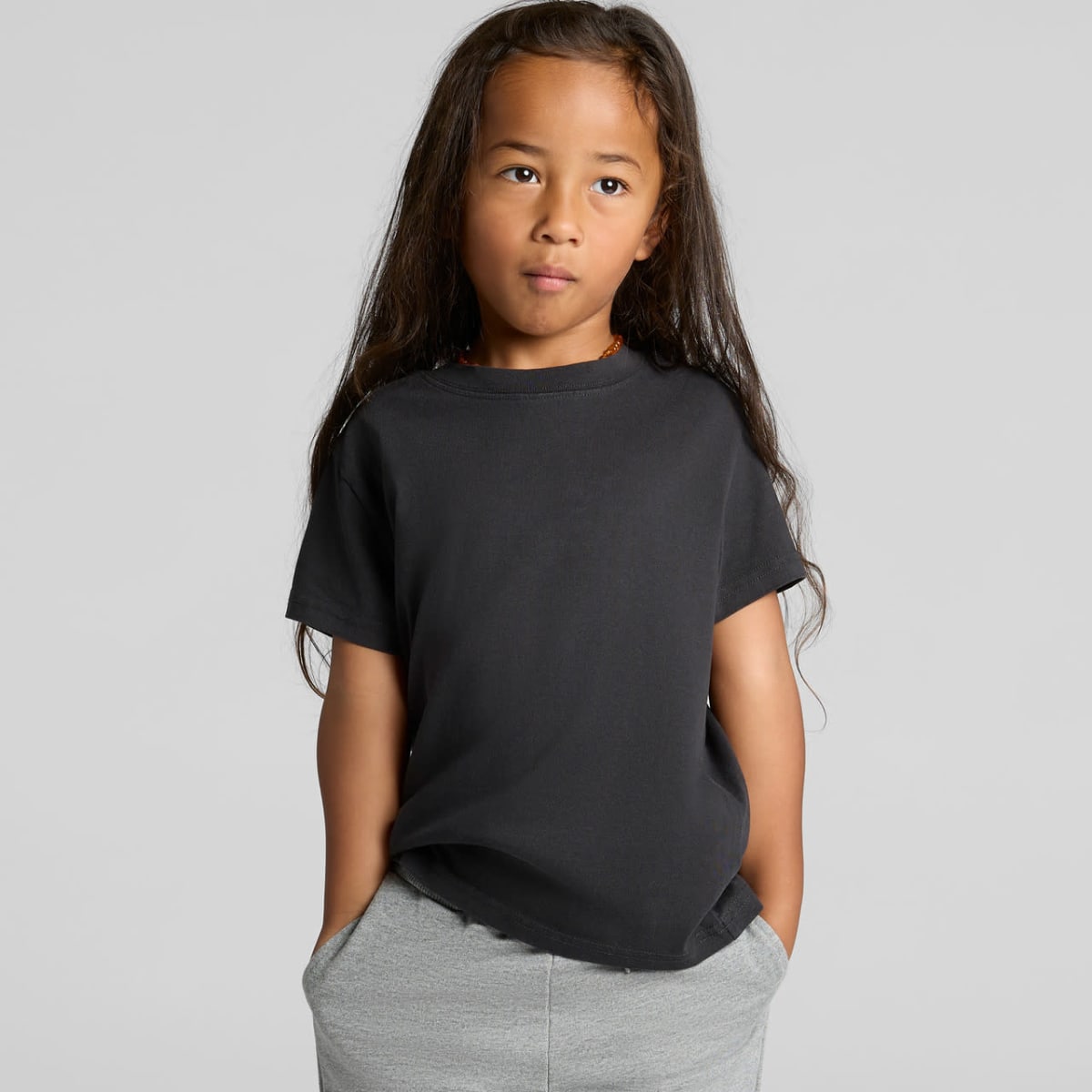 A child in a black t-shirt and gray pants stands with hands in pockets against a plain background.