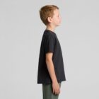 Young boy in a black t-shirt and green pants standing in profile against a gray background.