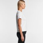 Woman in a white t-shirt and black pants standing in profile against a white background.