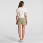 Woman standing facing away, wearing a white t-shirt, olive shorts, and white shoes.