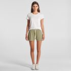 Woman standing facing forward, wearing a white t-shirt, green shorts, and white sneakers.