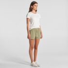 Woman in a white t-shirt, olive shorts, and sneakers standing against a plain background.