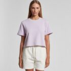 Woman in a light purple t-shirt and white shorts standing against a plain background.