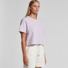 Woman in a light purple crop top and white shorts standing against a plain background.