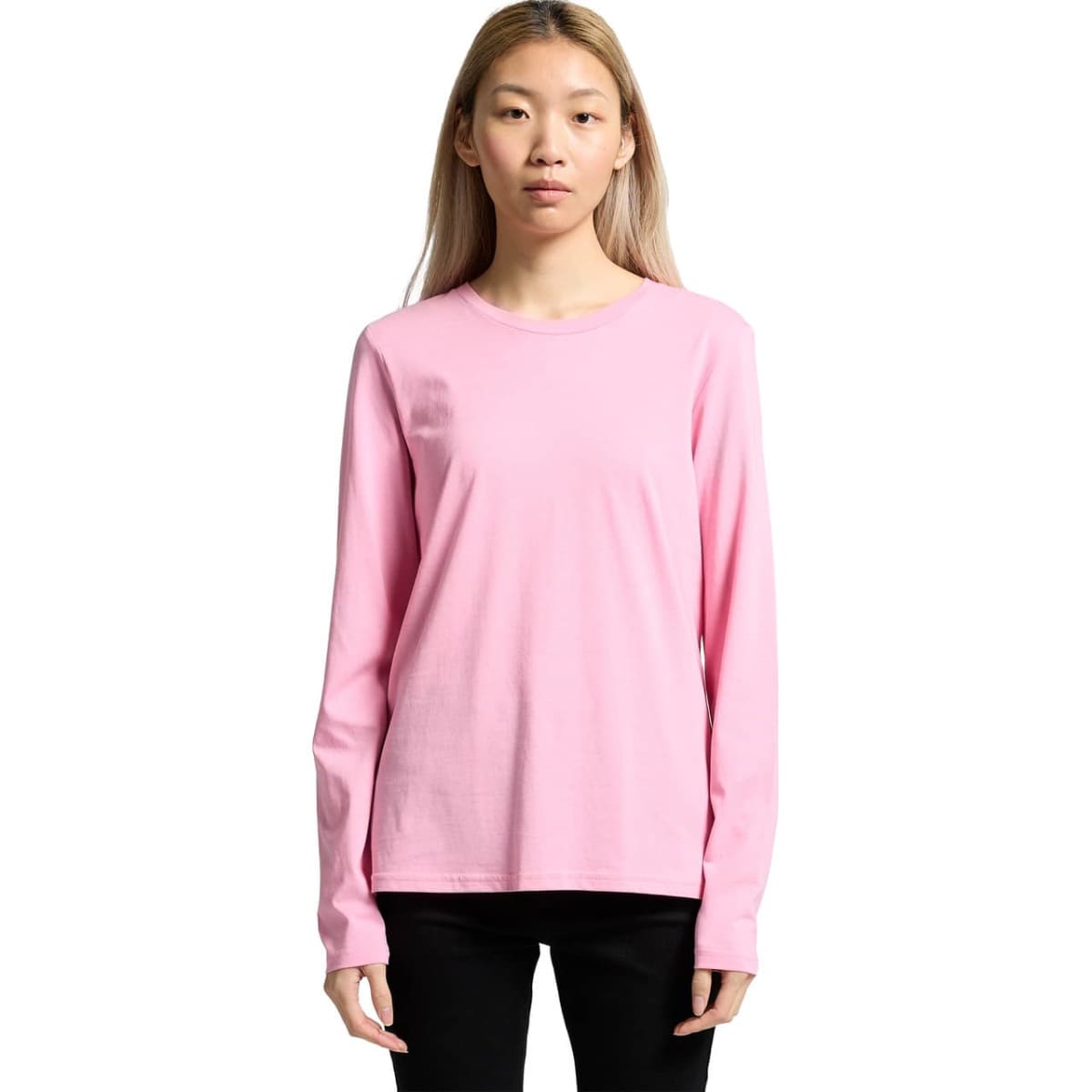 Person wearing a plain pink long-sleeve shirt and black pants, standing against white background.