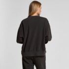 A woman with long blonde hair wears a loose black sweatshirt and pants, facing away.