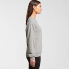 Woman in a gray sweatshirt and black pants standing in profile against a plain background.