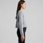 Woman in a gray cropped sweatshirt and black pants standing in profile against a plain background.