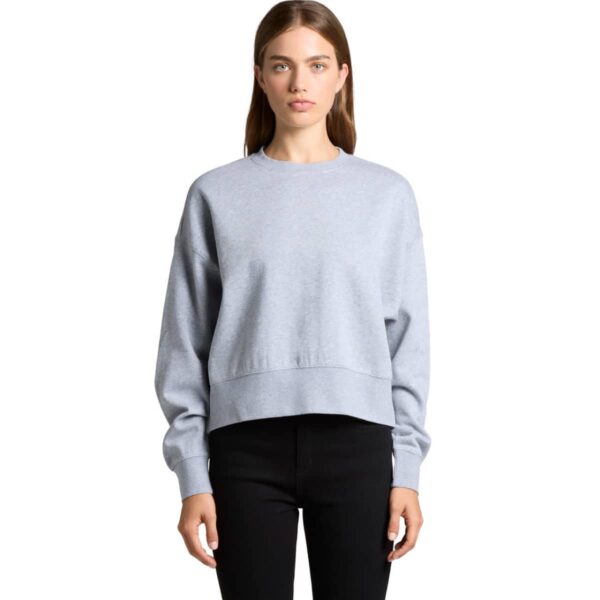 Woman wearing a light gray sweatshirt and black pants, standing against a white background.