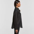 Woman in black long-sleeve shirt and pants standing in profile against a plain background.