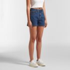 Woman wearing a white tank top, blue denim shorts, and white sneakers, standing upright.