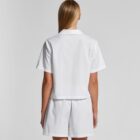 Person wearing a white short-sleeve shirt and shorts, seen from the back against a plain background.