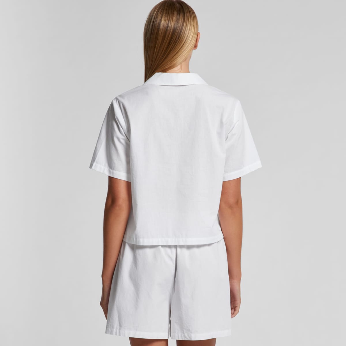 Person wearing a white short-sleeve shirt and shorts, seen from the back against a plain background.