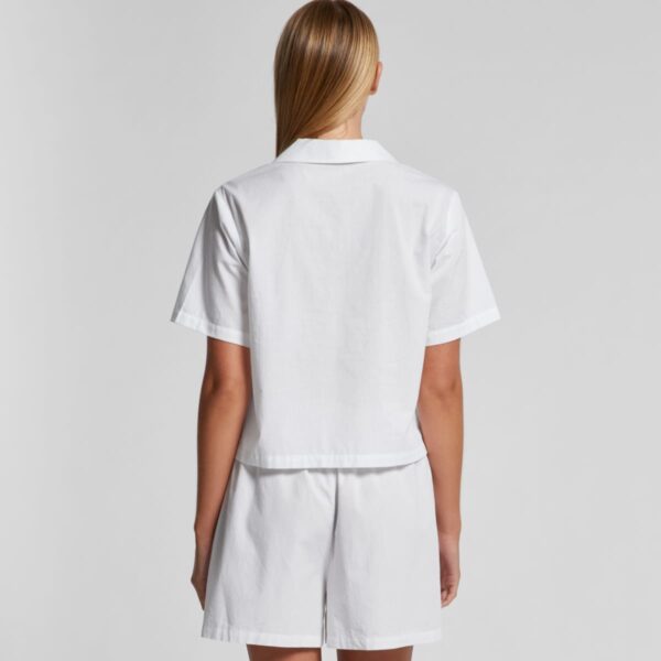 Person wearing a white short-sleeve shirt and shorts, shown from the back against gray background.