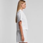 Woman in white short-sleeve shirt and shorts, standing in profile against a plain background.