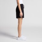 Person in a white shirt, black shorts, and white sneakers standing in profile view.