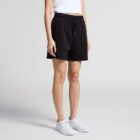 Person wearing black shorts, white top, and white sneakers standing against a plain background.