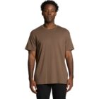 Man standing and wearing a plain brown t-shirt and black pants against a white background.