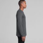 Man in a gray long-sleeve shirt standing sideways against a plain light background.
