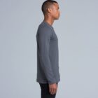 Man in a grey long-sleeve shirt standing sideways against a plain light background.