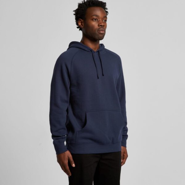 Man wearing a navy blue hoodie and black pants stands against a plain light gray background.