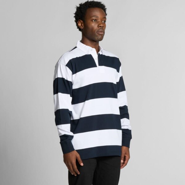 Man wearing a navy and white striped long-sleeve polo shirt, standing against a gray background.