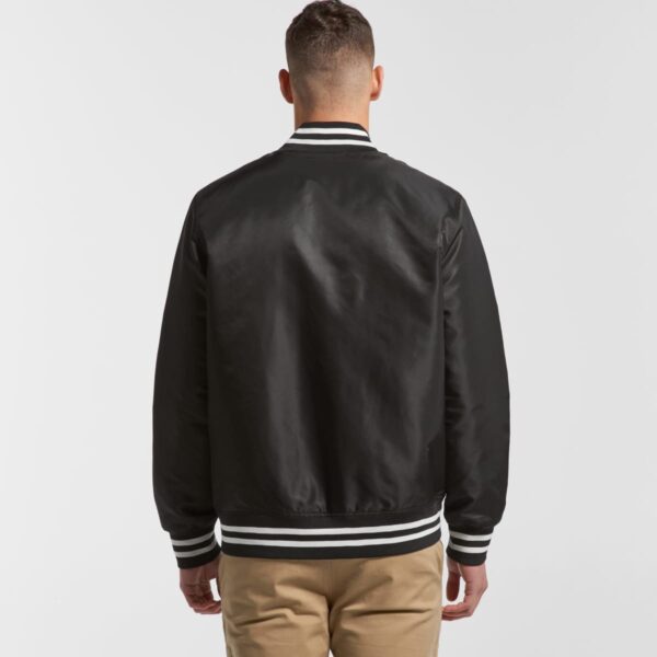 Man wearing a black varsity jacket and khaki pants, shown from the back.