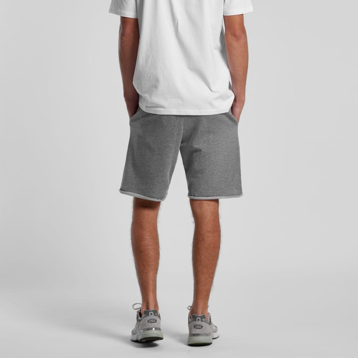 Person standing in gray shorts, white t-shirt, and gray sneakers, seen from behind.