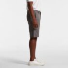 Man in gray shorts, white shirt, and white sneakers standing sideways against white background.