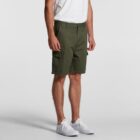 Man wearing olive green cargo shorts, white t-shirt, and white sneakers, standing.