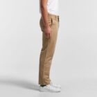 A person in khaki pants and white sneakers stands sideways against a plain background.