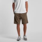 Man wearing a white t-shirt, brown shorts, and gray sneakers, standing with hands in pockets.