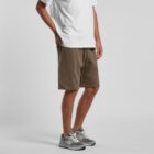 Person wearing a white T-shirt, brown shorts, and gray sneakers standing on a plain background.