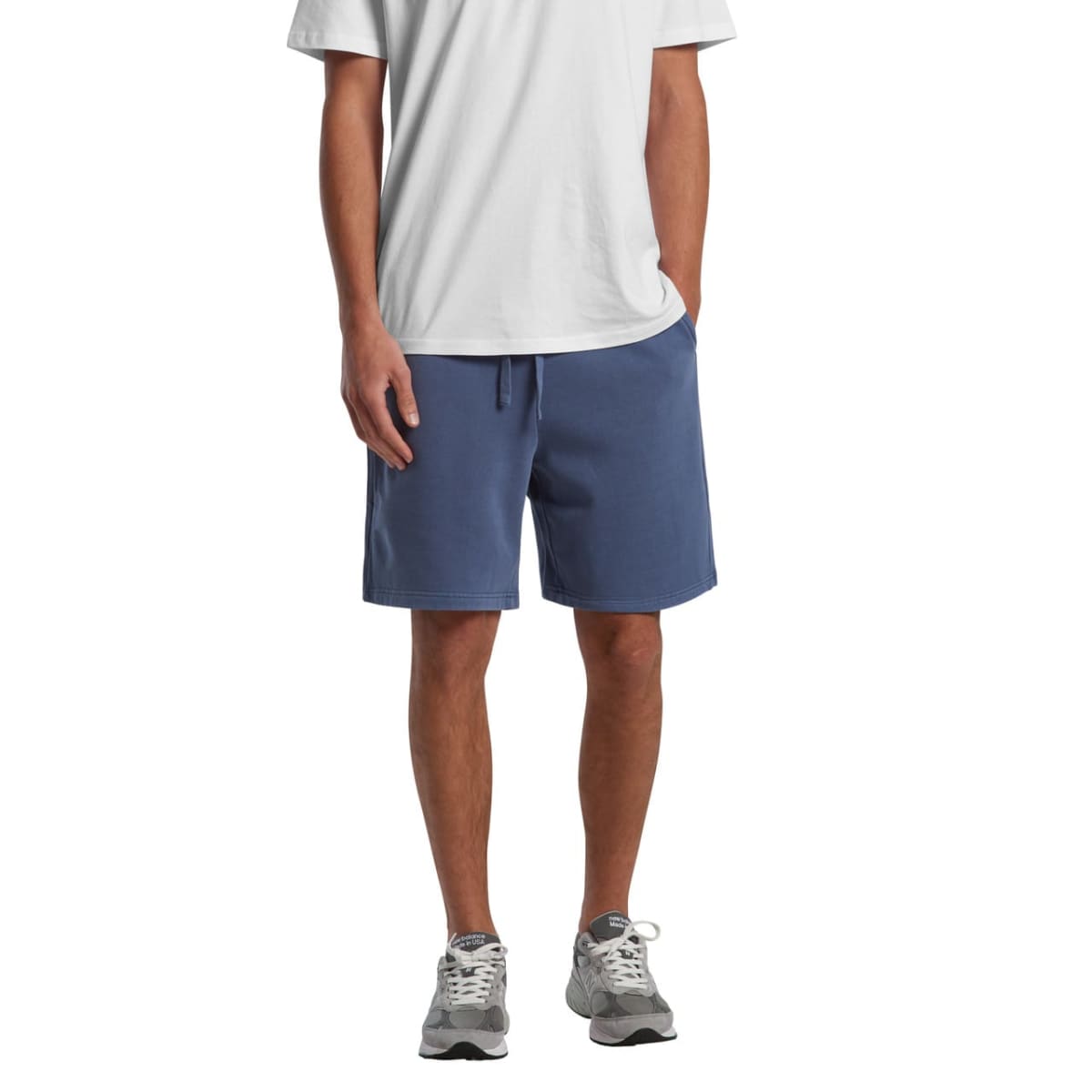 Man in a white t-shirt, blue shorts, and gray sneakers standing against a white background.