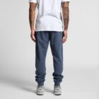 Person in blue joggers, white t-shirt, and sneakers standing with back facing the camera.
