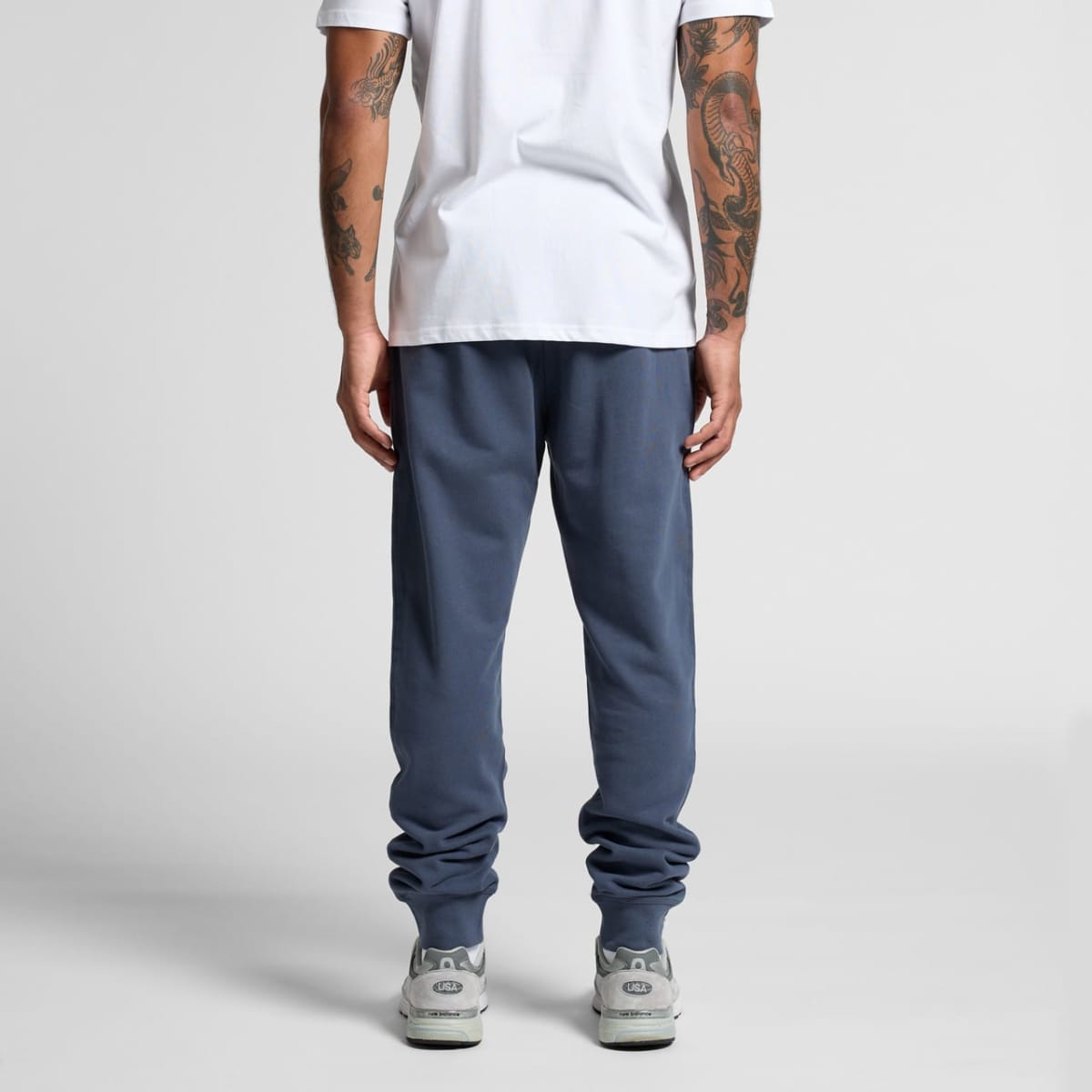 Person in blue joggers, white t-shirt, and sneakers standing with back facing the camera.