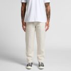 Person in white t-shirt, cream pants, and black sneakers standing against plain background.