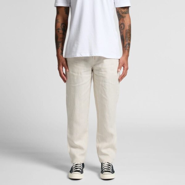 Person wearing a white t-shirt, beige pants, and black sneakers, standing against a plain background.